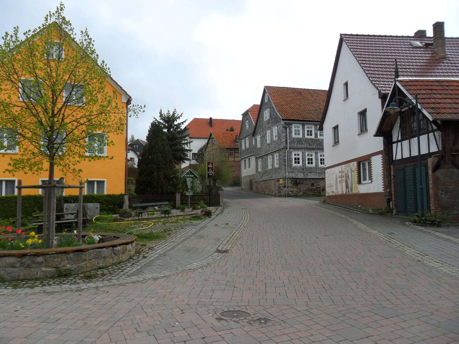 Gepflasterte Dorfstraße in Bechstedt mit Fachwerkhäusern und bepflanztem Brunnen