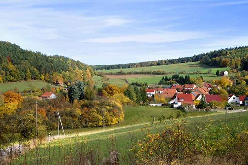 Bechstedt im Herbst: rote Dächer zwischen goldenem Laub, eingebettet in Wiesen und bewaldete Hänge