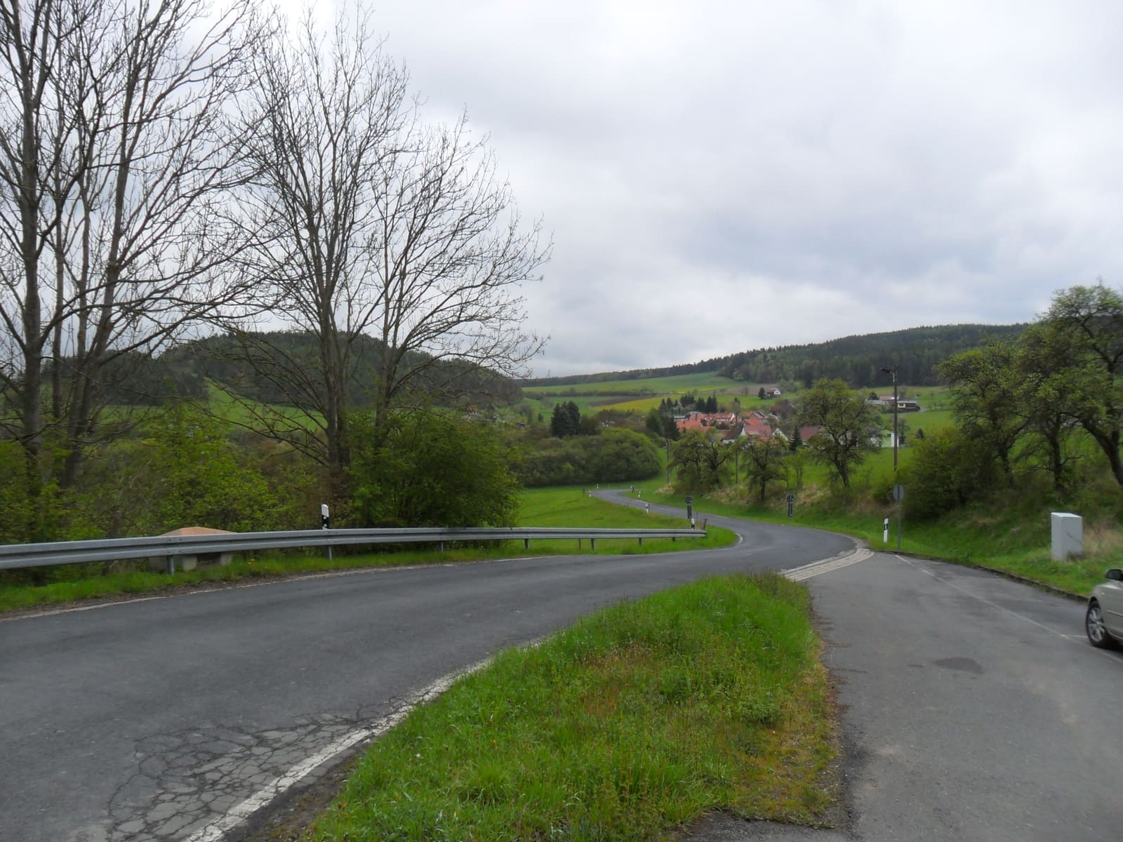 Landstraße nach Bechstedt, die sich durch Wiesen und Waldrand zum Ort hinabschwingt
