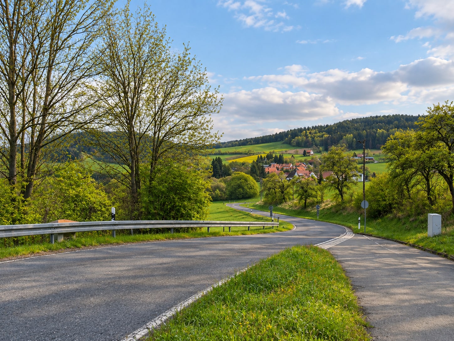 Landstraße nach Bechstedt, die sich durch Wiesen und Waldrand zum Ort hinabschwingt