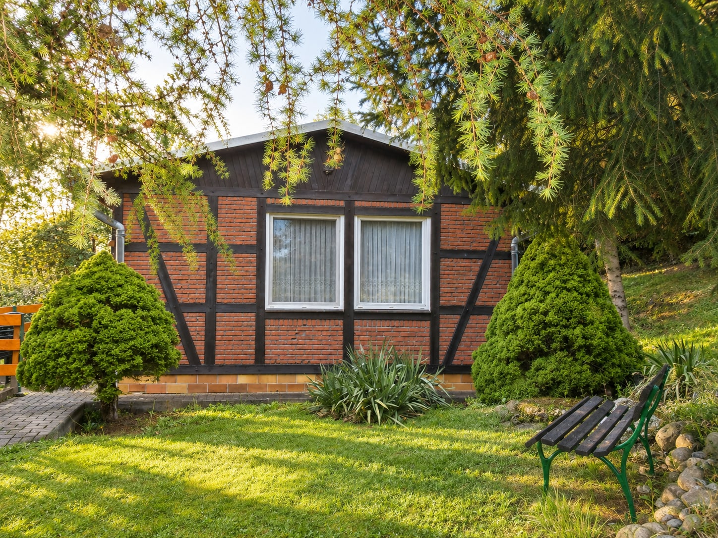 Der Bungalow von außen: Fachwerkfassade, gepflegter Rasen und eine Bank unter alten Bäumen