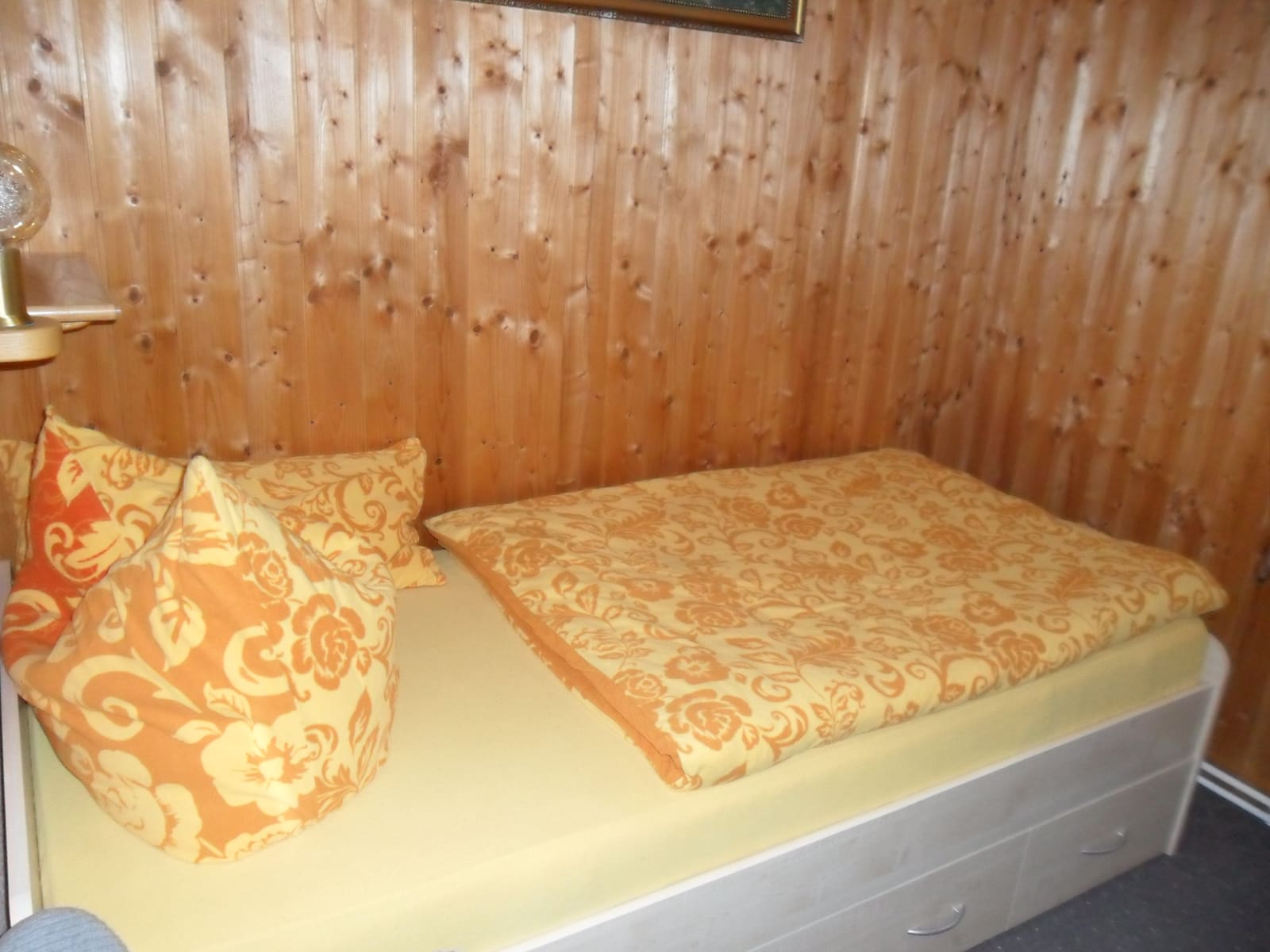 Weiteres Bett im Bungalow mit gelber Tagesdecke vor Holzwand