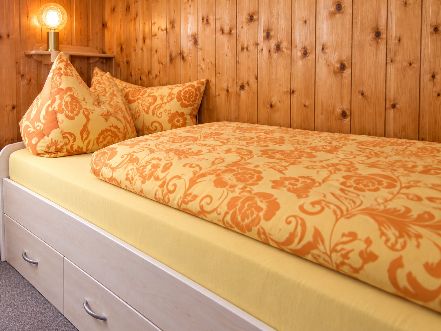 Weiteres Bett im Bungalow mit gelber Tagesdecke vor Holzwand