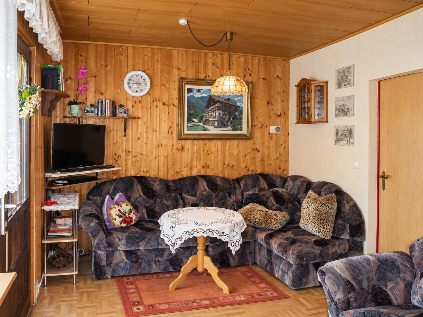 Wohnraum im Bungalow mit Polstergarnitur, Fernseher und heller Holzvertäfelung