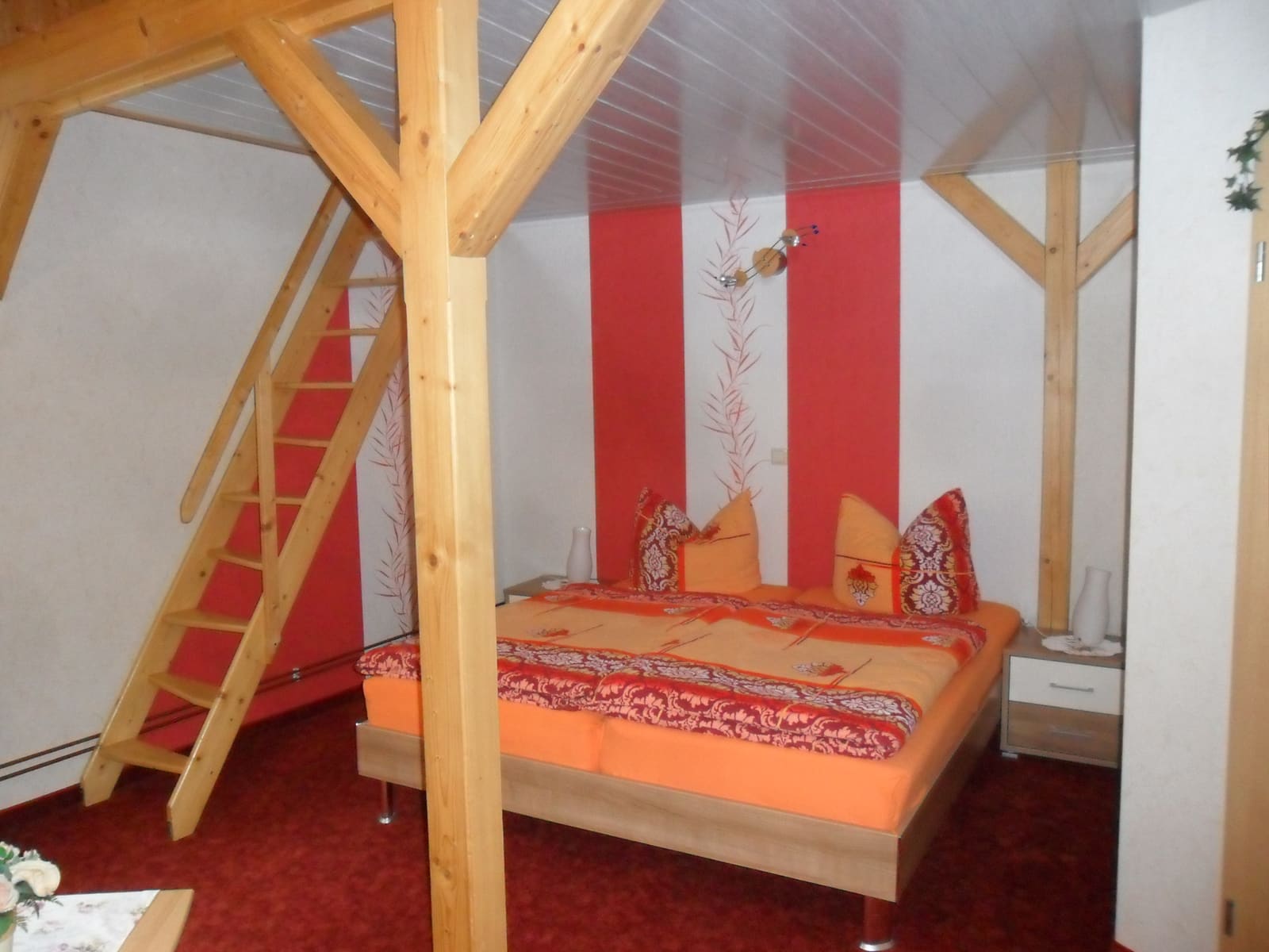 Schlafzimmer des zweiten Appartements mit Doppelbett, Holzbalken und offener Treppe