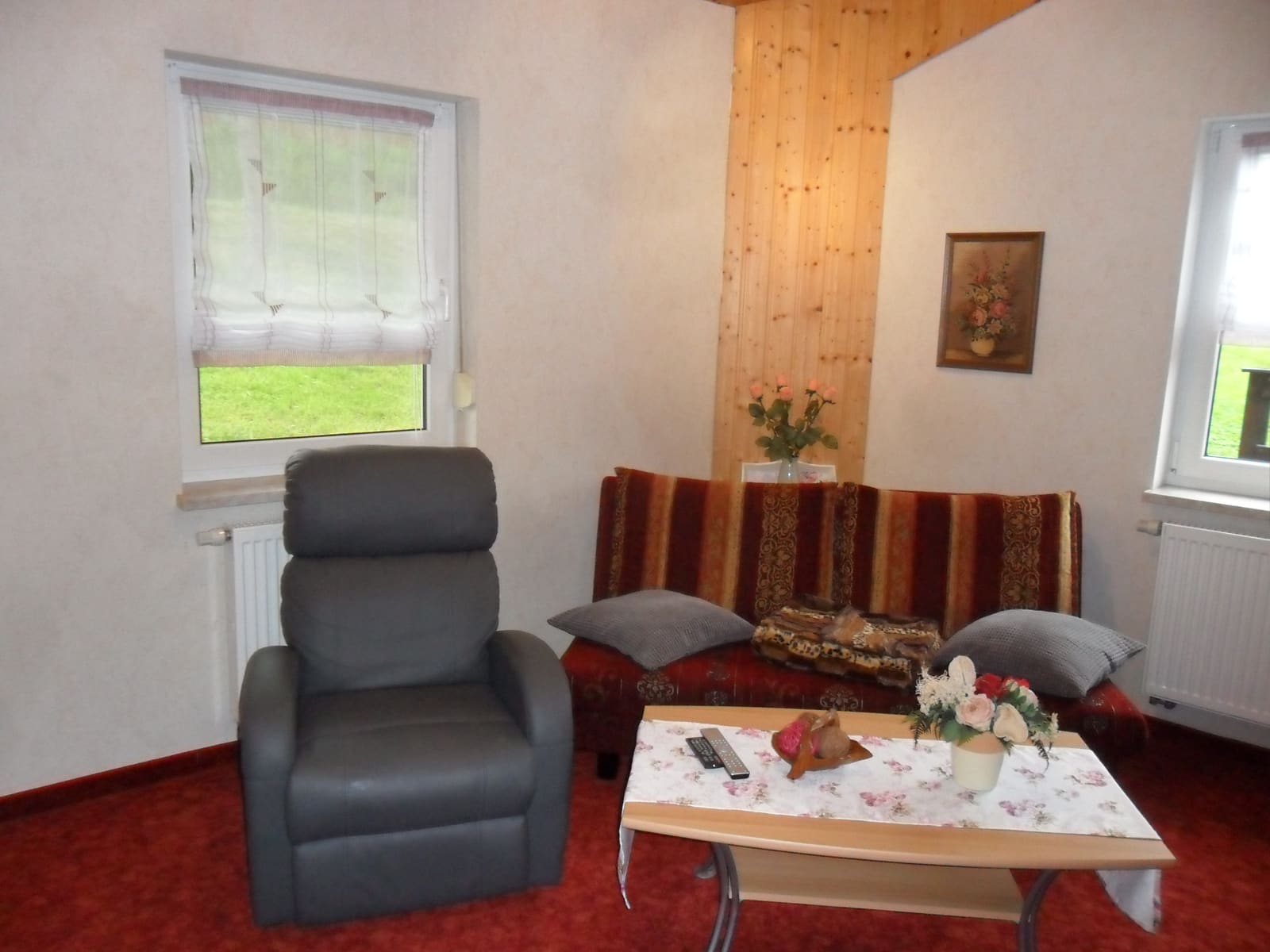 Wohnraum des zweiten Appartements mit Relaxsessel, Sitzecke und rotem Teppichboden