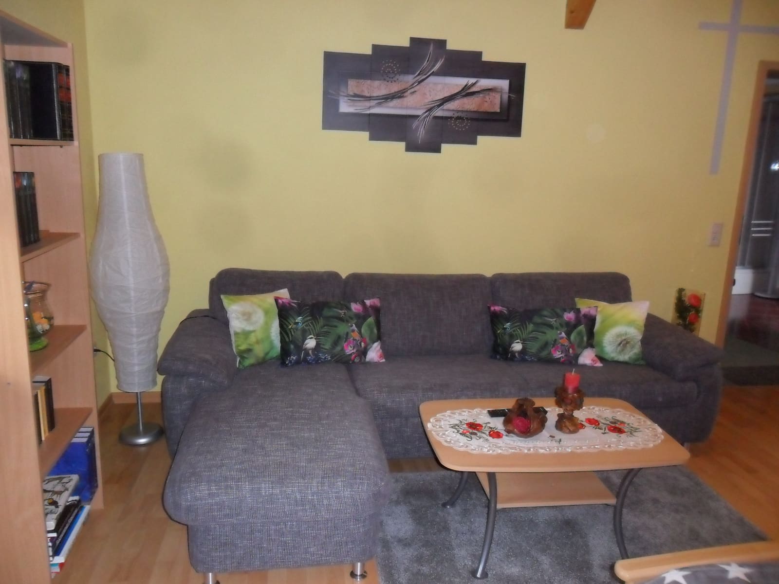 Wohnzimmer der Ferienwohnung mit grauer Eckcouch, Couchtisch und gelber Wand