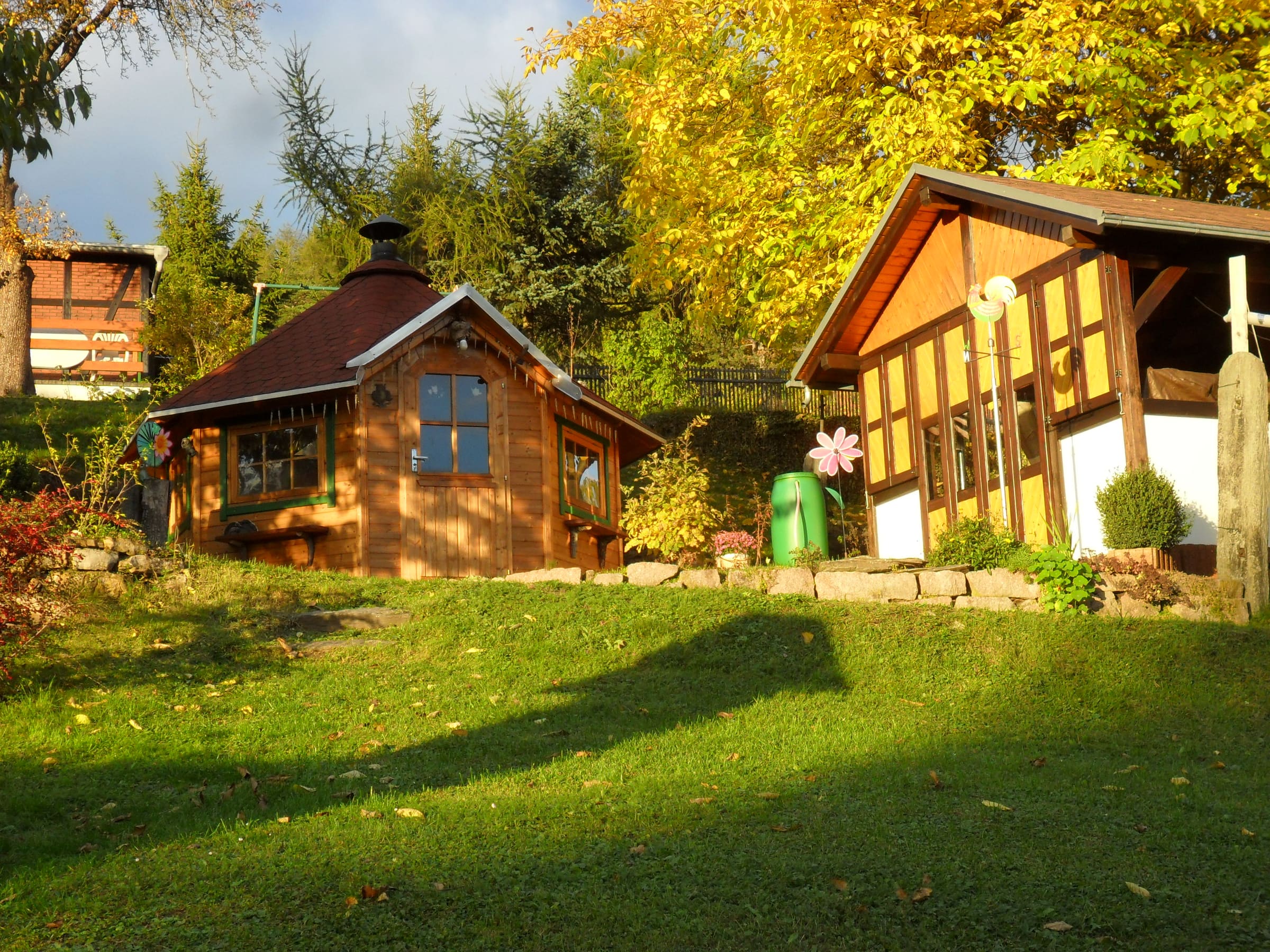 Grillkota und Gartenhaus im goldenen Herbstlicht auf der Wiese hinter dem Haus
