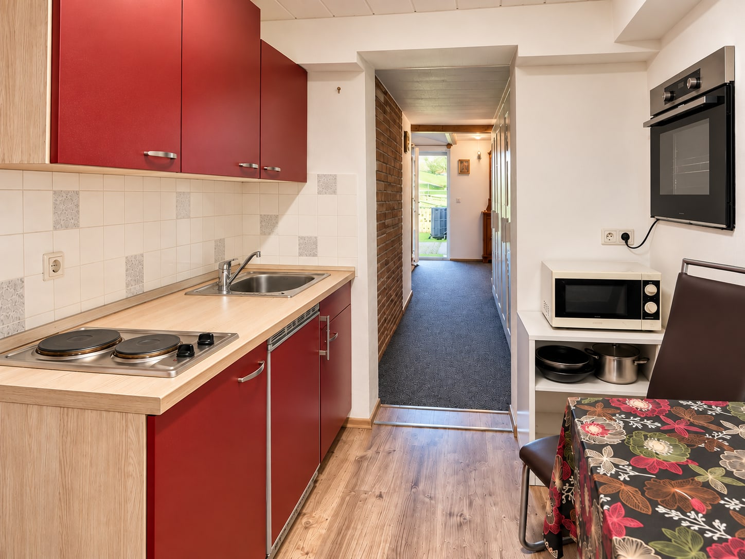 Rote Küchenzeile der Single-Wohnung mit Kochfeld, Spüle und Essplatz