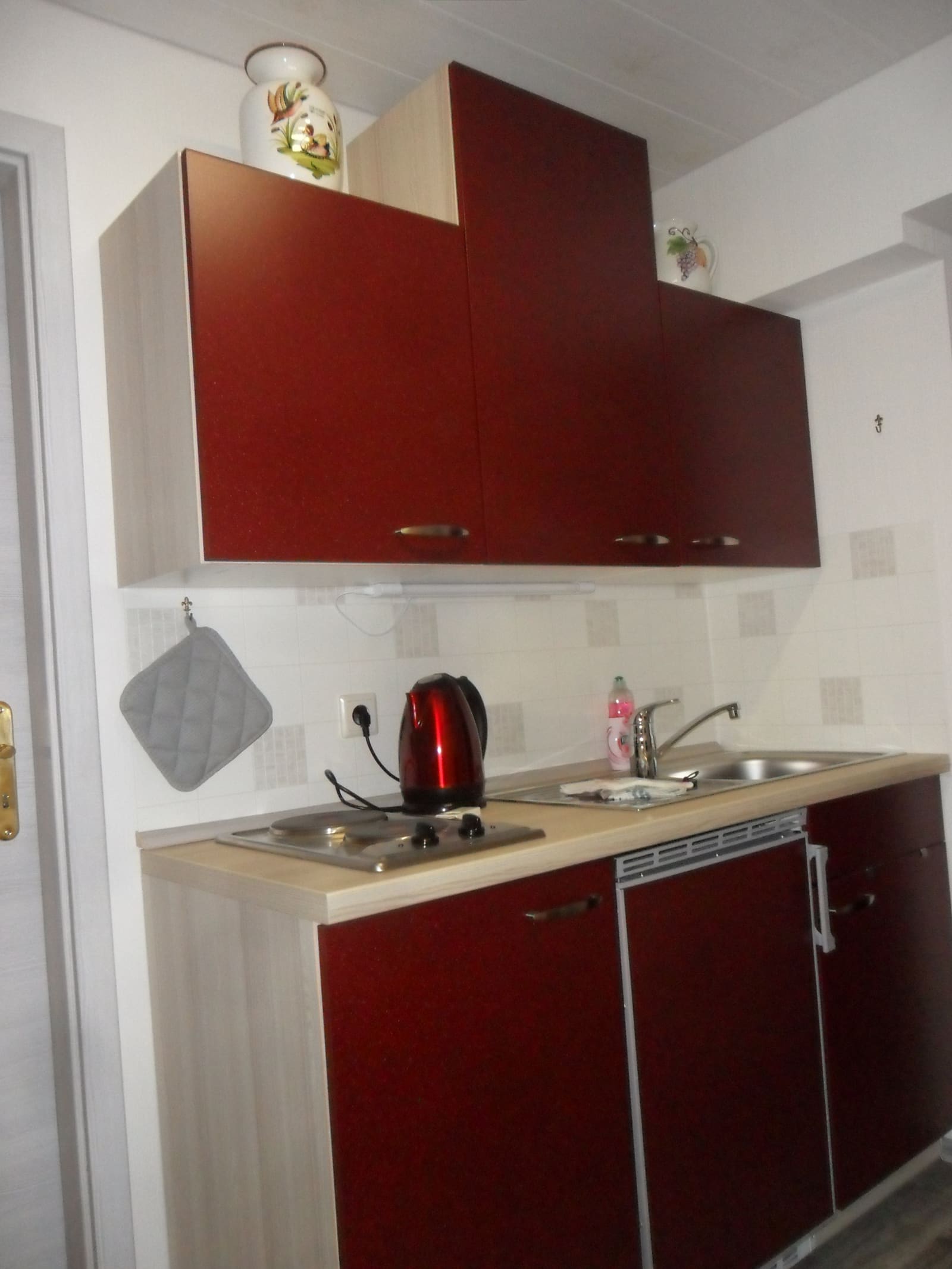 Rote Küchenzeile der Single-Wohnung mit Spüle, Kochfeld und Oberschränken