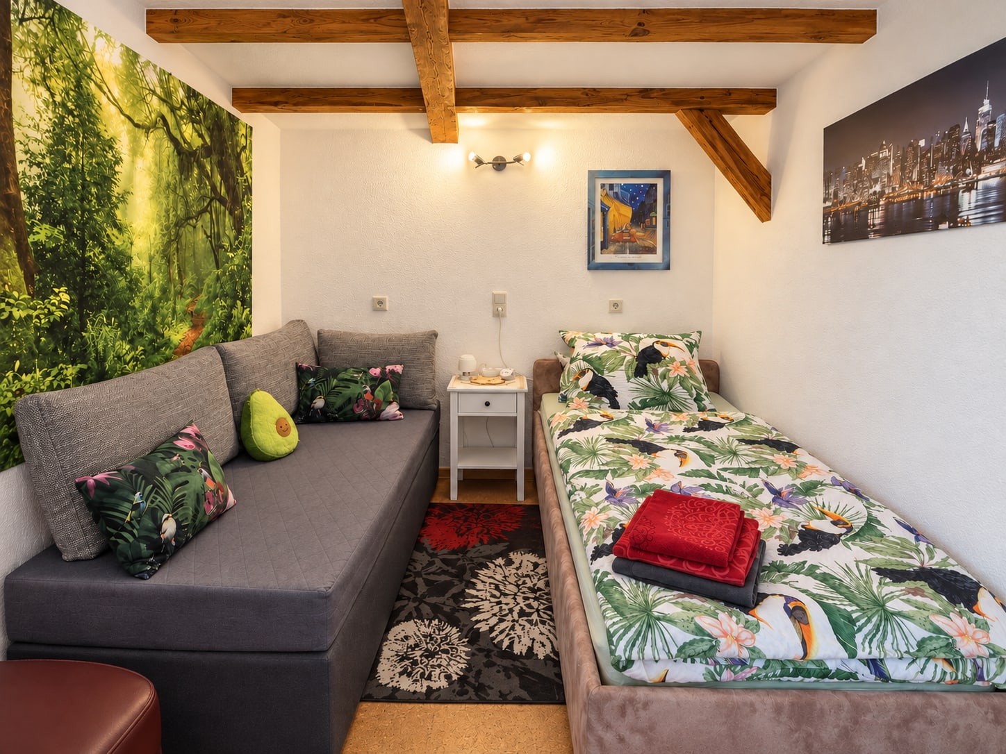 Schlafraum der Single-Wohnung mit Einzelbett, grauem Sofa und Waldmotiv an der Wand