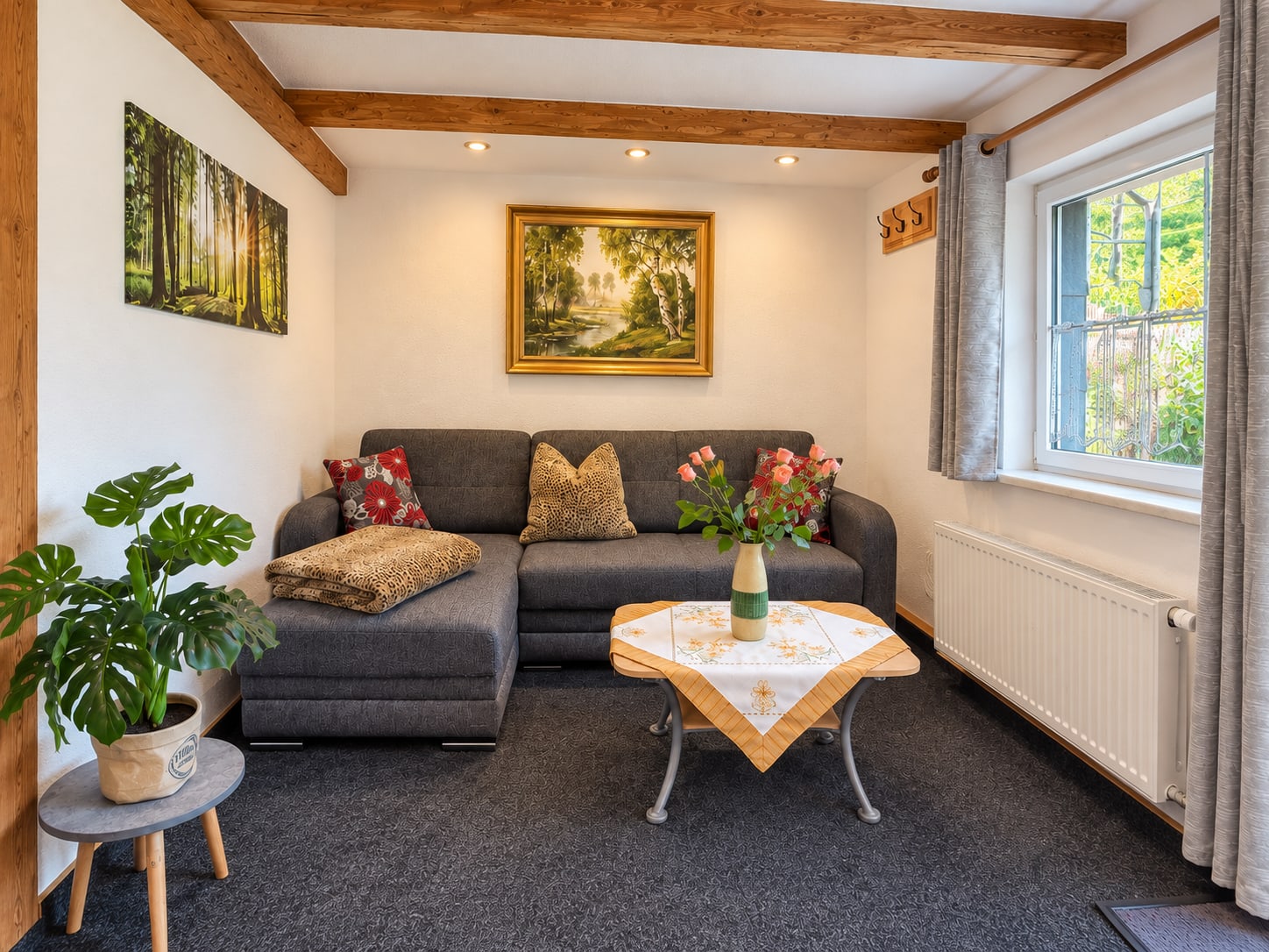 Wohnzimmer der Single-Wohnung mit grauem Ecksofa, Holzbalken und Fenster zum Garten